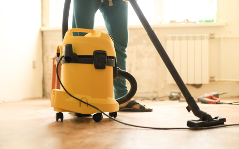 A young man vacuums the floor with a construction vacuum cleaner.