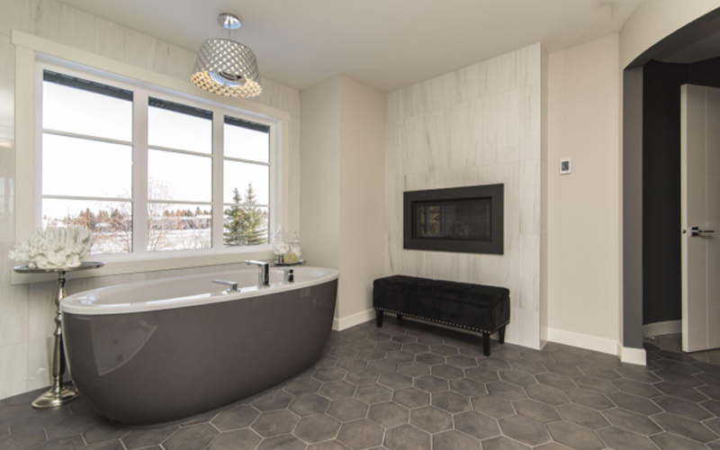 Modern bathroom with grey tub, fireplace, large windows, and hexagonal LVT floor.