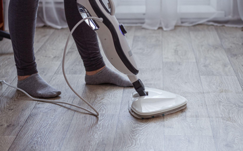 A young woman washes the floor with a modern steam cleaner. 