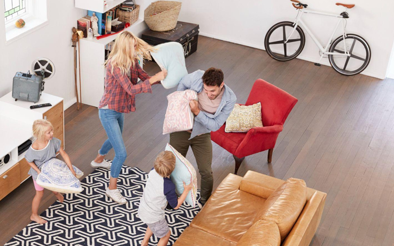 Parents playing with their children in a lounge with wooden floors.