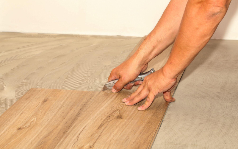 A man is installing luxury vinyl tile (LVT) flooring.