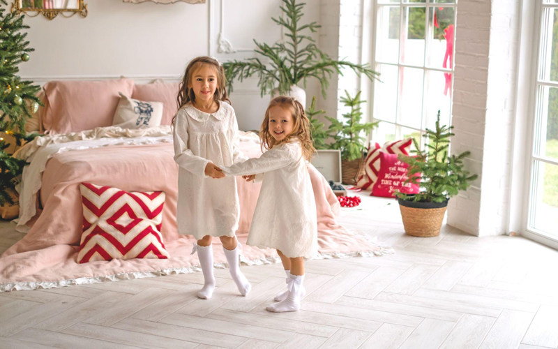 The girls are standing hand in hand on the herringbone-patterned white oak floor in the bedroom.