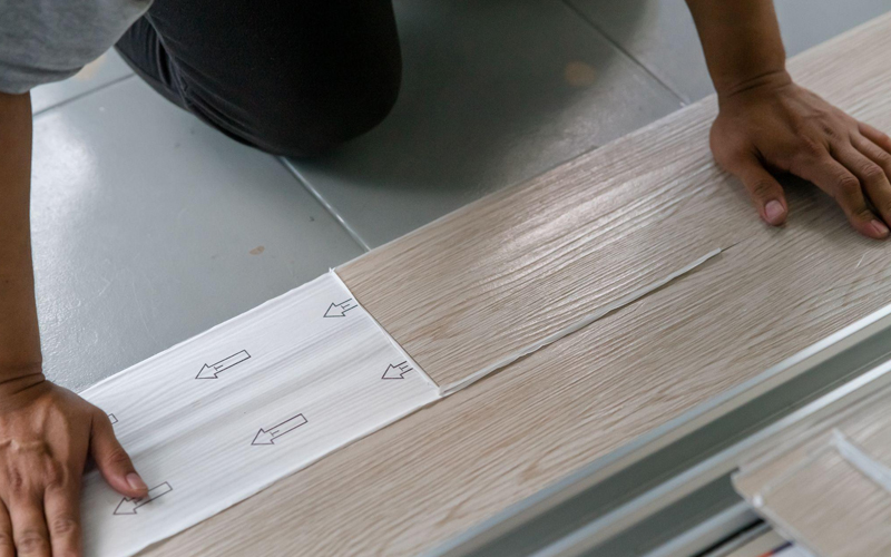 A worker is installing self-adhesive vinyl flooring.
